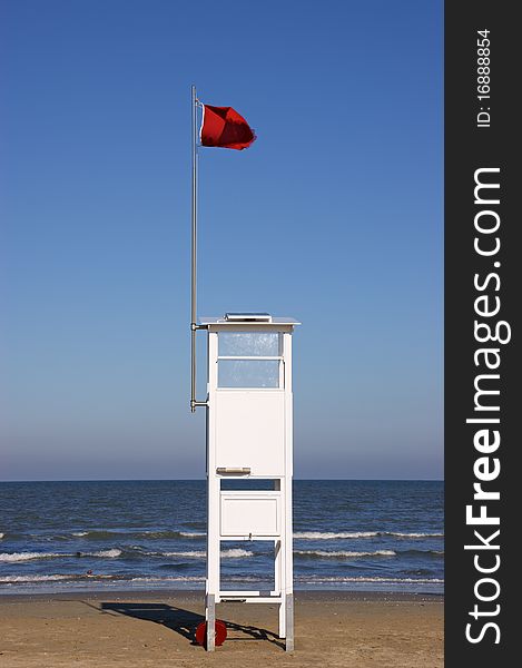 Lifeguard tower on the beach with a red warning flag