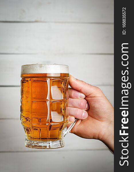 Male Hand Holding A Full Beer Mug On White Wooden Background. Toned Ima