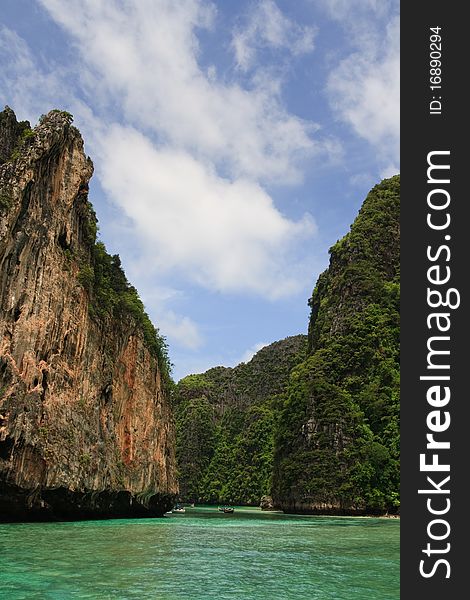 Long Tail Boat passing between dramatic tropical sea cliffs, Maya Beach, Ko Phi Phi Lei, Thailand. Long Tail Boat passing between dramatic tropical sea cliffs, Maya Beach, Ko Phi Phi Lei, Thailand