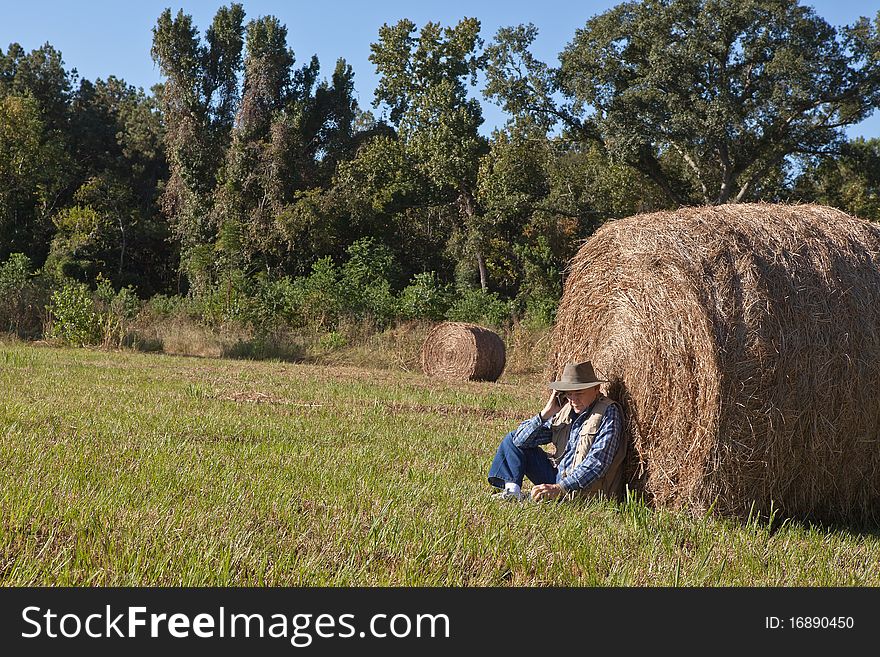 Mature man sitting next to a bale of hay and talking on phone. Mature man sitting next to a bale of hay and talking on phone.
