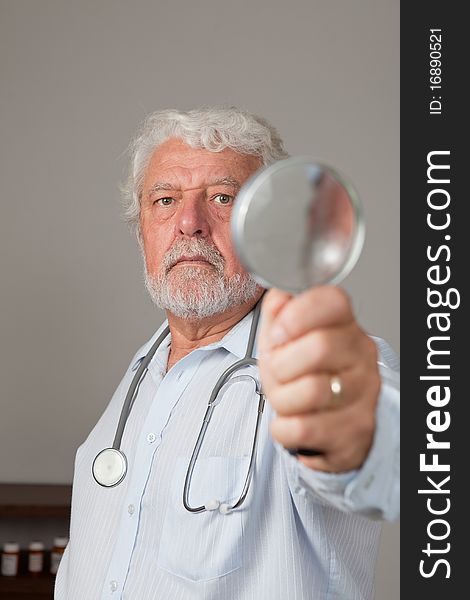 Mature man with stethoscope and holding a magnifying glass. Could be a doctor looking at an x-ray. Focus on eyes. Mature man with stethoscope and holding a magnifying glass. Could be a doctor looking at an x-ray. Focus on eyes.