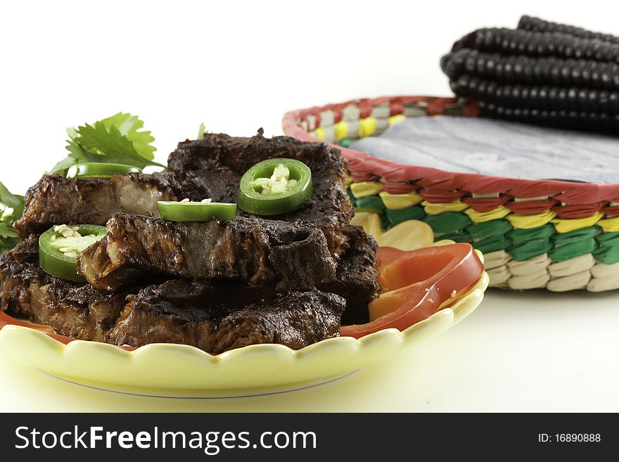 Beef short ribs barbecued with Mexican adobe sauce on a plate with jalapeno peppers and cilantro garnish and blue corn tortillas in a basket. Beef short ribs barbecued with Mexican adobe sauce on a plate with jalapeno peppers and cilantro garnish and blue corn tortillas in a basket.