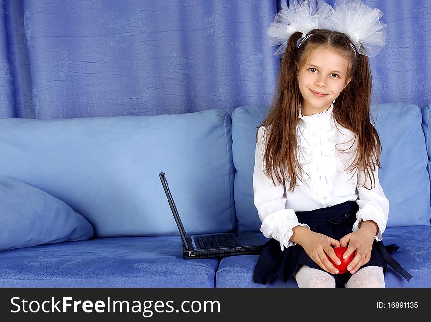 Schoolgirl with laptop and red apple in sofa