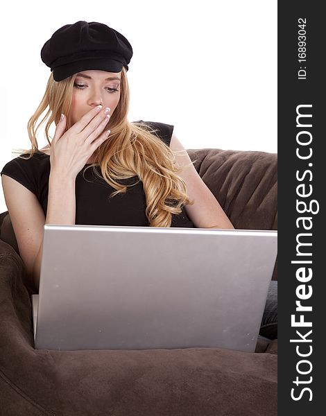 A woman in a black hat is yawning and using a computer. A woman in a black hat is yawning and using a computer.