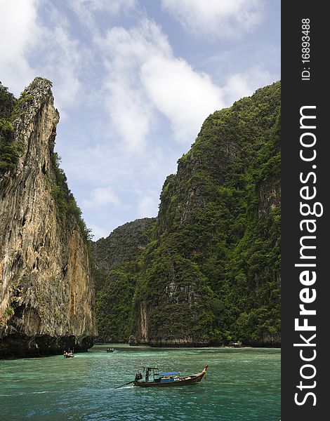 Long Tail Boat passing between dramatic tropical sea cliffs, Maya Beach, Ko Phi Phi Lei, Thailand. Long Tail Boat passing between dramatic tropical sea cliffs, Maya Beach, Ko Phi Phi Lei, Thailand