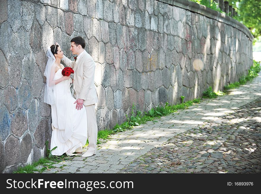 Bride in white dress and groom near old wall. Bride in white dress and groom near old wall
