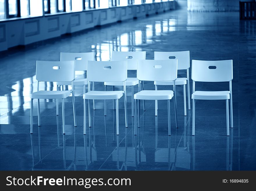 Few white plastic chairs standing in big hallway. Blue tone. Few white plastic chairs standing in big hallway. Blue tone