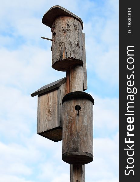 Three wooden starling-houses on background with blue sky and clouds. Three wooden starling-houses on background with blue sky and clouds