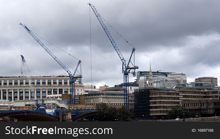 the banks of the thames. on the left side of the river a construction site and its cranes at work.