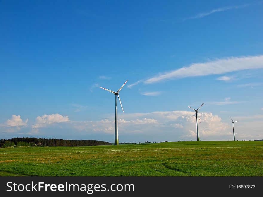 Three windmills standing on a large green field