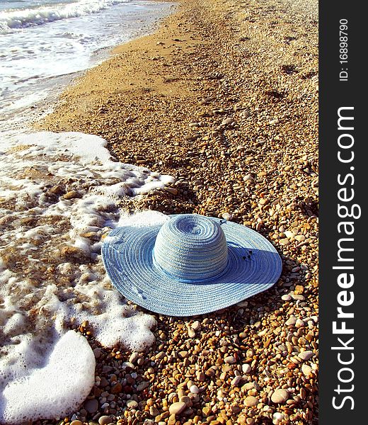 Sea and blue women`s hat on a shingle beach