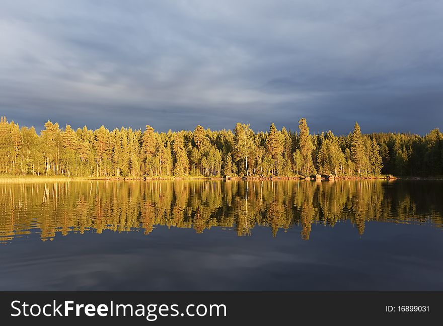 Storm clouds as the sun shines on the forest by a lake. Storm clouds as the sun shines on the forest by a lake.