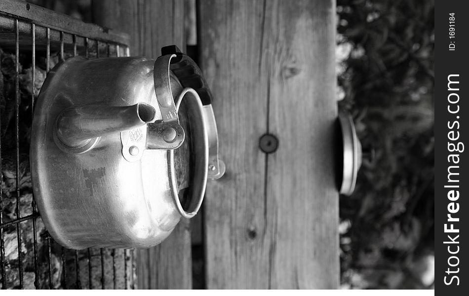 Monochrome picture of a aluminium kettle boiling over a charcoal fire on a wooden bench. Inside is tea bags. . Monochrome picture of a aluminium kettle boiling over a charcoal fire on a wooden bench. Inside is tea bags.