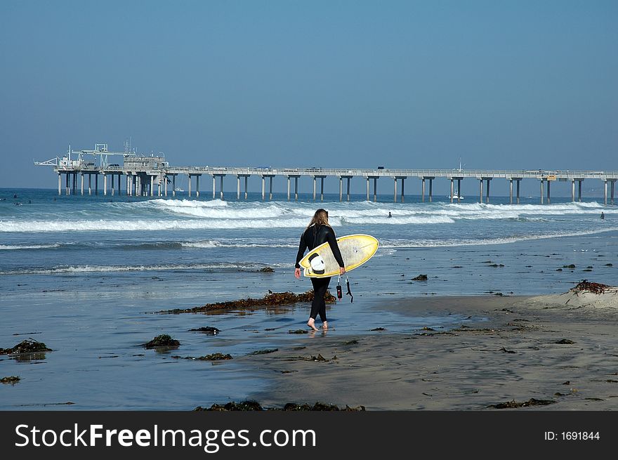 Surfer walking on the beach toward pier. Surfer walking on the beach toward pier