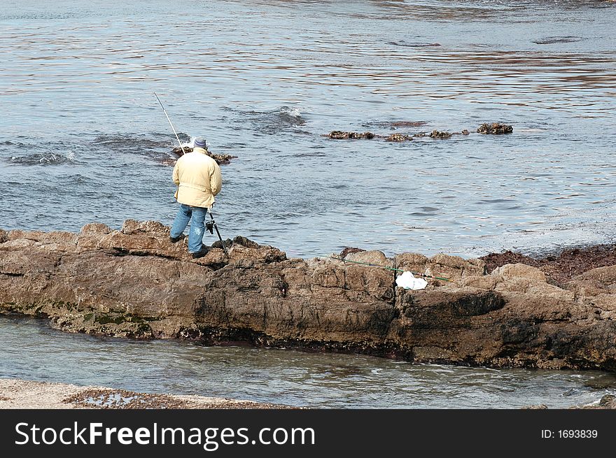 Man fishing alone over rocks in front of sea. Man fishing alone over rocks in front of sea