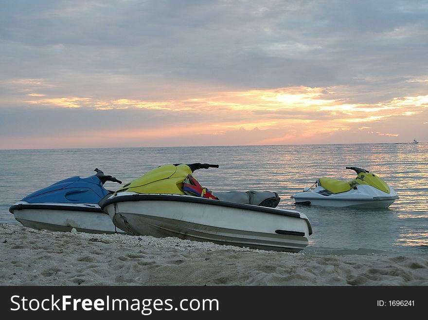 Three jet skies on the sand at sunset time with a boat passing on the background. Three jet skies on the sand at sunset time with a boat passing on the background