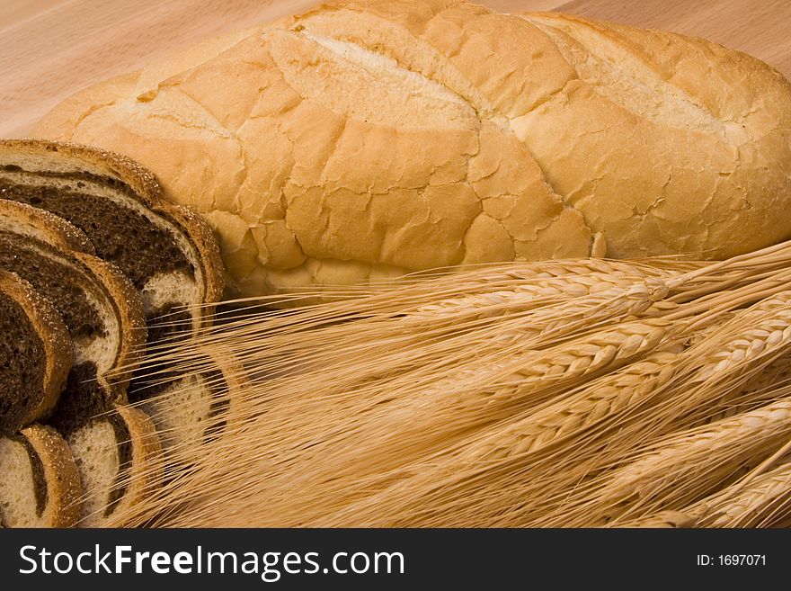 Close up of two different kinds of bread and some wheat on a wood cutting board. Close up of two different kinds of bread and some wheat on a wood cutting board
