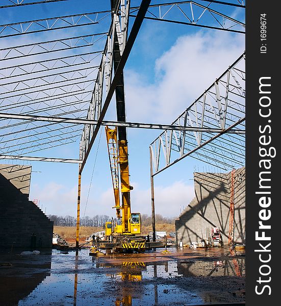 A yelow crane on a construction site with a blue sky background. A yelow crane on a construction site with a blue sky background