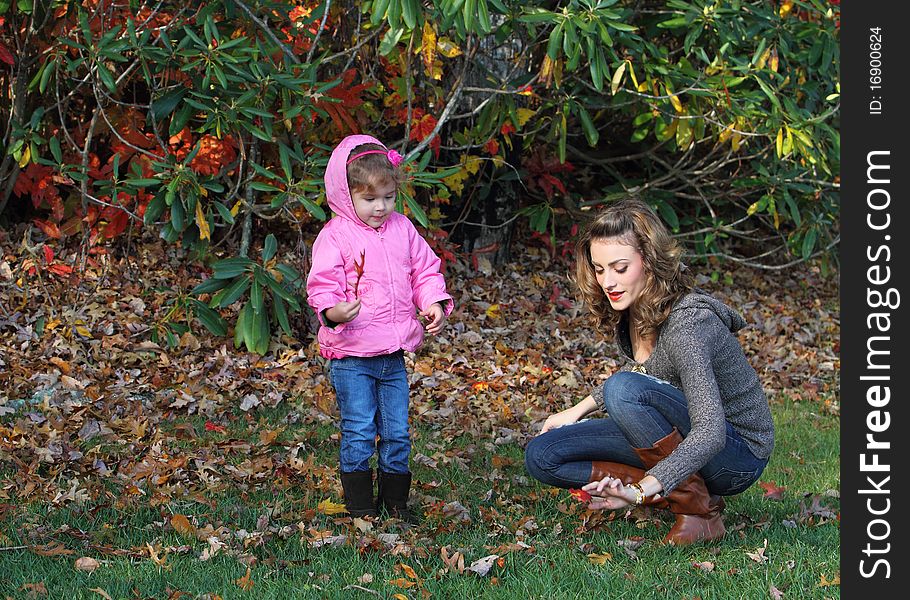 Mother and girl are playing with fall leaves