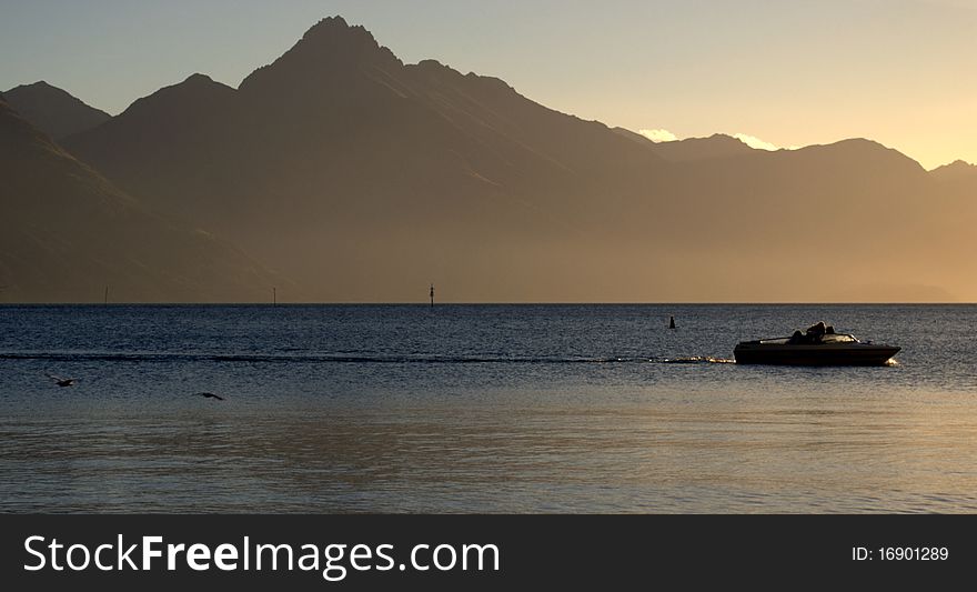 A boat calmly floats on Lake Wakatipu during dusk in Queenstown, New Zealand. A boat calmly floats on Lake Wakatipu during dusk in Queenstown, New Zealand.