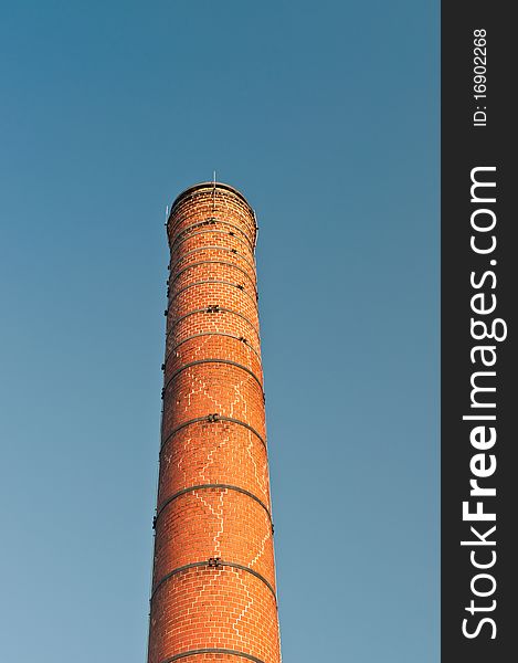 An old brick chimney reinforced with metal bands stands out against a blue sky. An old brick chimney reinforced with metal bands stands out against a blue sky.