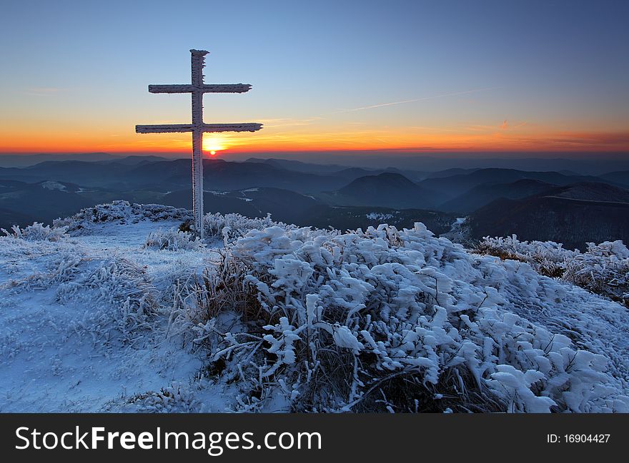 A frosty sunset in mountains with cross