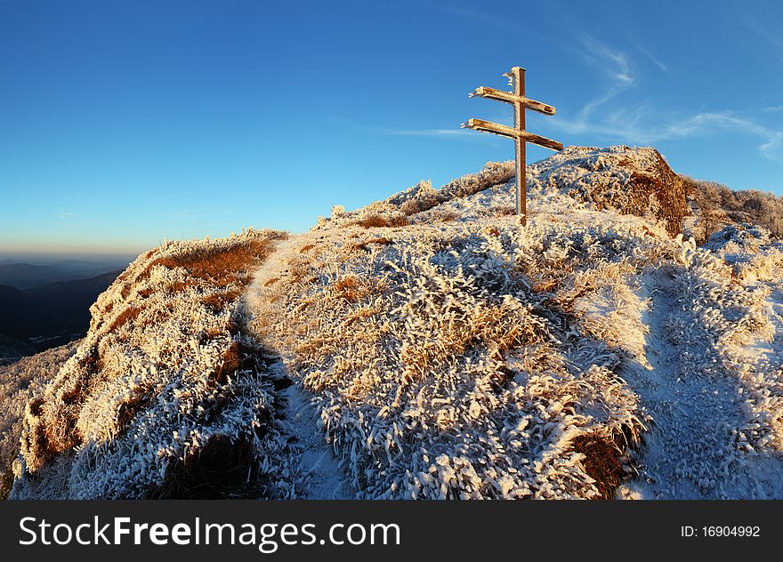 A frosty sunset in mountains with cross