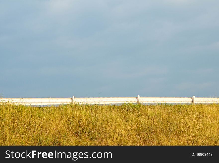 The white fence in between of blue sky and green field. The white fence in between of blue sky and green field