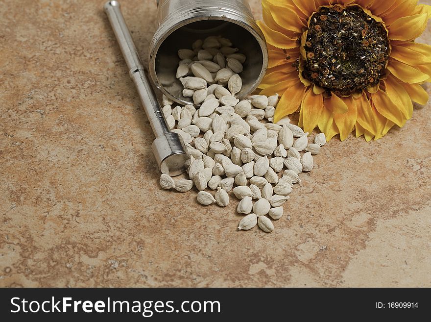 Cardamom seeds white with a sunflower on brown tile with mortar and pedestal.