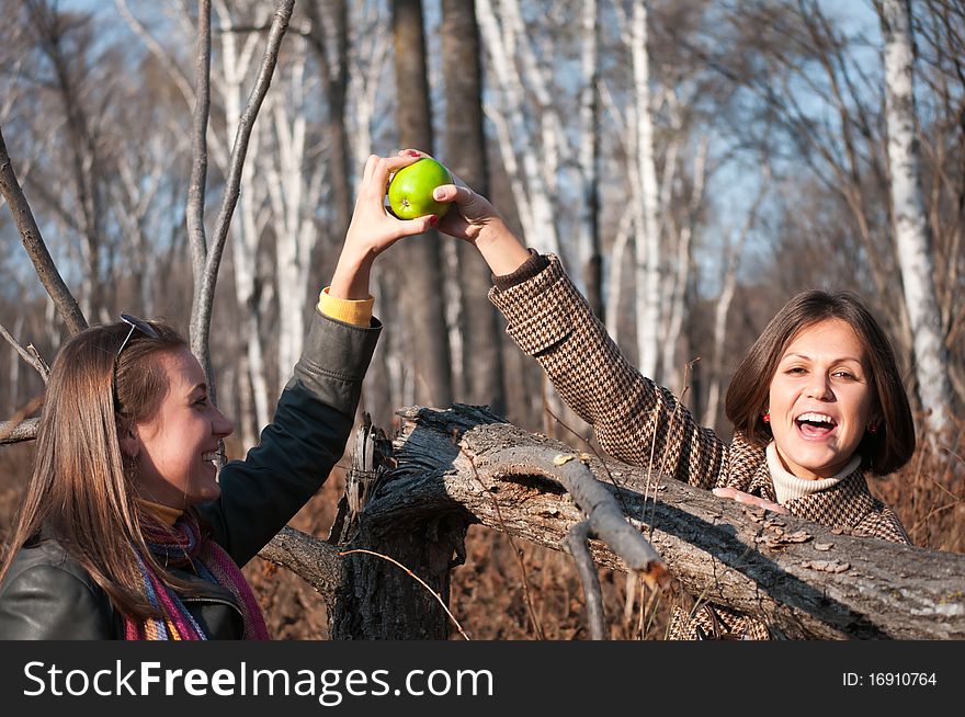 Two young beautiful women playing with green apple in the autumn forest. Two young beautiful women playing with green apple in the autumn forest