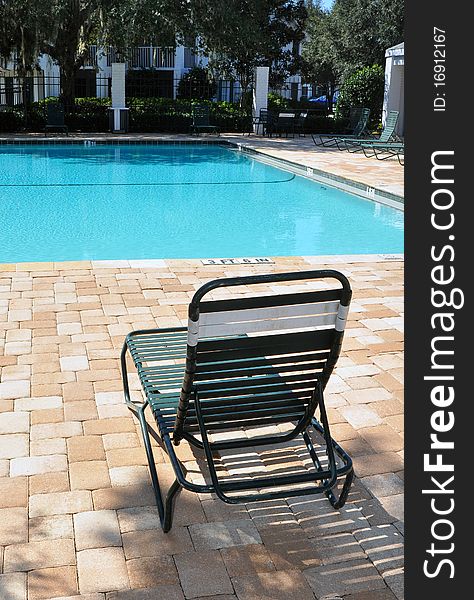 Green pool chair made from metal and rubber, in front of a swimming pool, vertical view. Green pool chair made from metal and rubber, in front of a swimming pool, vertical view