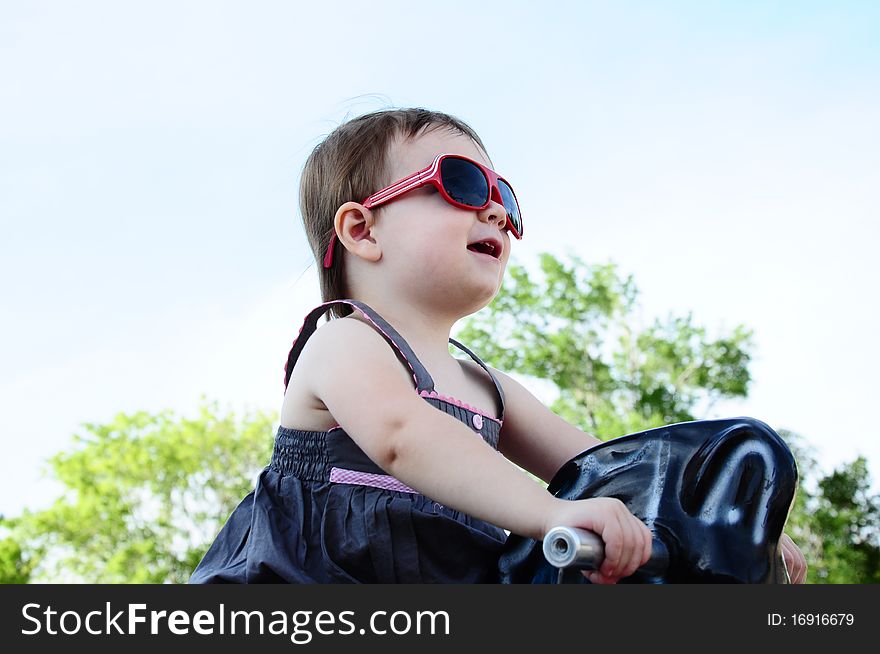 Little girl at park riding horse with sunglasses