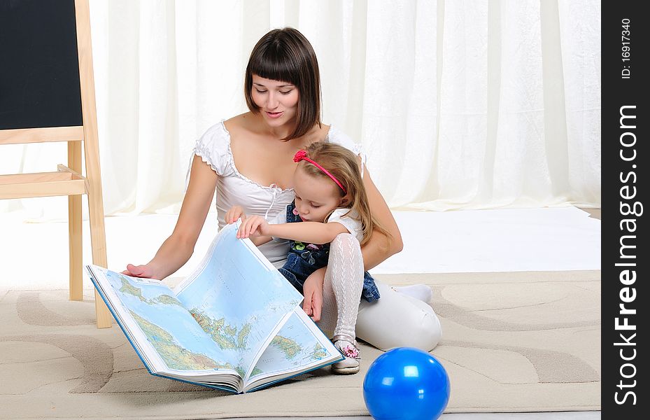 Young mother and her daughter studying geography with atlas