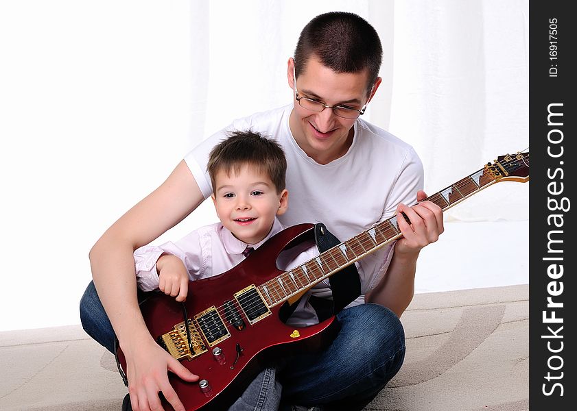 A young father teaches his young son to play guitar