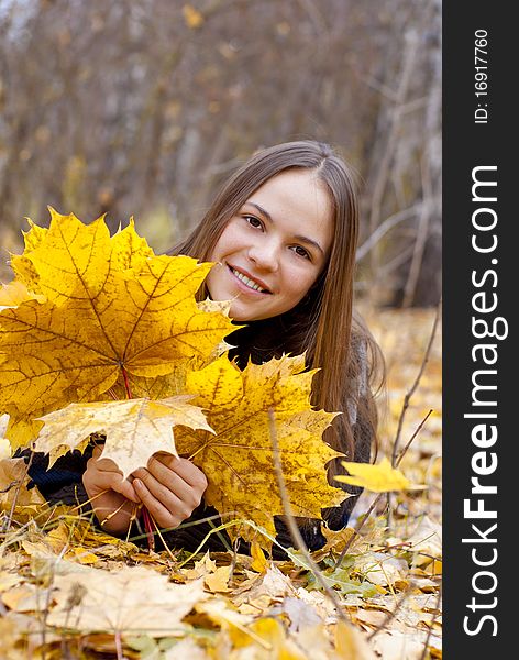 Portrait of smiling girl in autumn park laying on leaves.