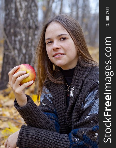 Portrait of brown-haired girl in autumn park with apple. Portrait of brown-haired girl in autumn park with apple