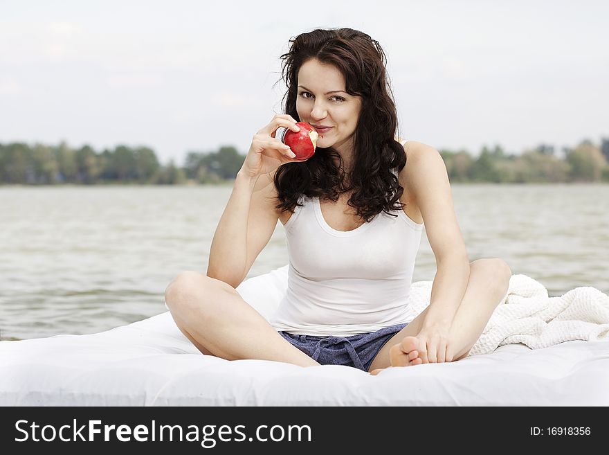 Beautiful young woman with apple lying on the white bed in the sea. Beautiful young woman with apple lying on the white bed in the sea