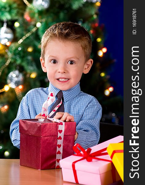 Happy little boy opening Christmas gifts near New Year's tree