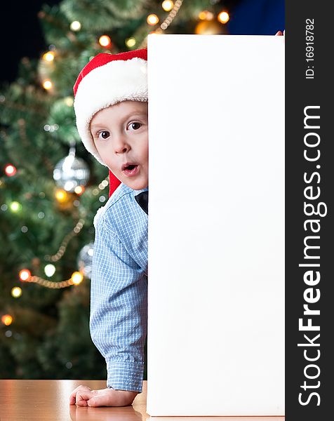 4 years old boy holding blank near New Year's tree with expression on his face. 4 years old boy holding blank near New Year's tree with expression on his face