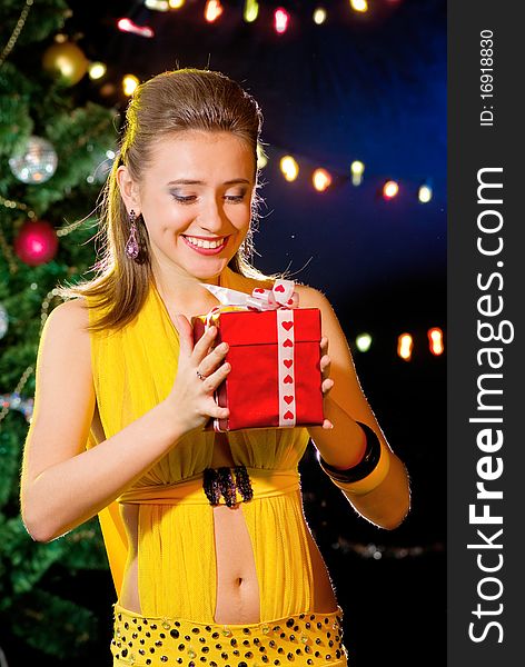 Attractive woman holding Christmas gift in red box near the New year's tree