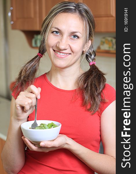 Portrait of young happy woman eating salad at domestic kitchen. Portrait of young happy woman eating salad at domestic kitchen