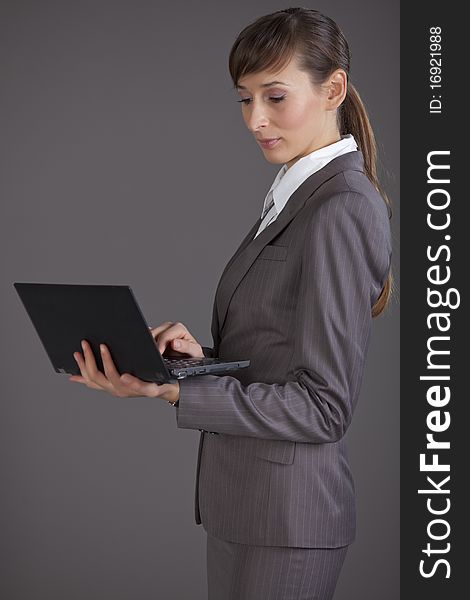 Portrait of business woman holding small computer over grey background. Portrait of business woman holding small computer over grey background
