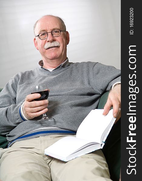 Senior man is reading a book with a glass wine in his hand