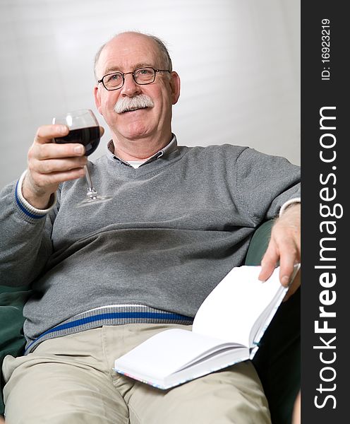 Senior man is reading a book with a glass wine