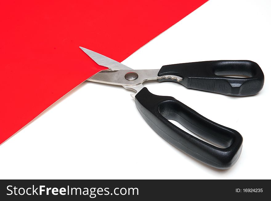 Black scissors is cutting a red cardboard