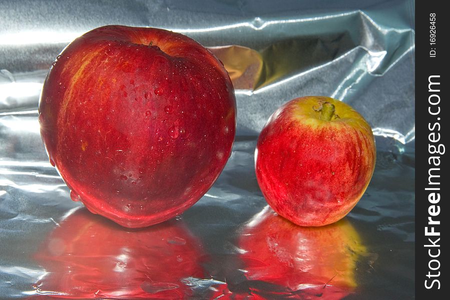 A macro image of two newly picked apples on a reflective surface. A macro image of two newly picked apples on a reflective surface.