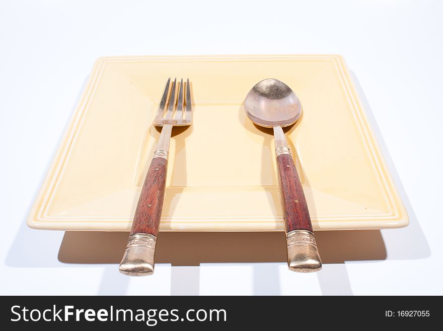Orange square shaped plate with spoon and fork is placed on a white background. Orange square shaped plate with spoon and fork is placed on a white background.