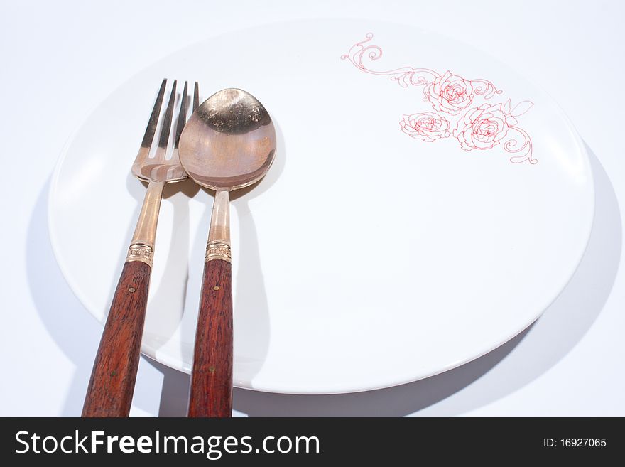 Round white plate with spoon and fork is placed on a white background. Round white plate with spoon and fork is placed on a white background.