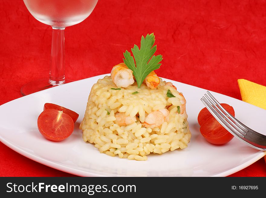 Risotto with shrimps served on a white plate and decorated with cherry tomatoes. Studio shot over red background