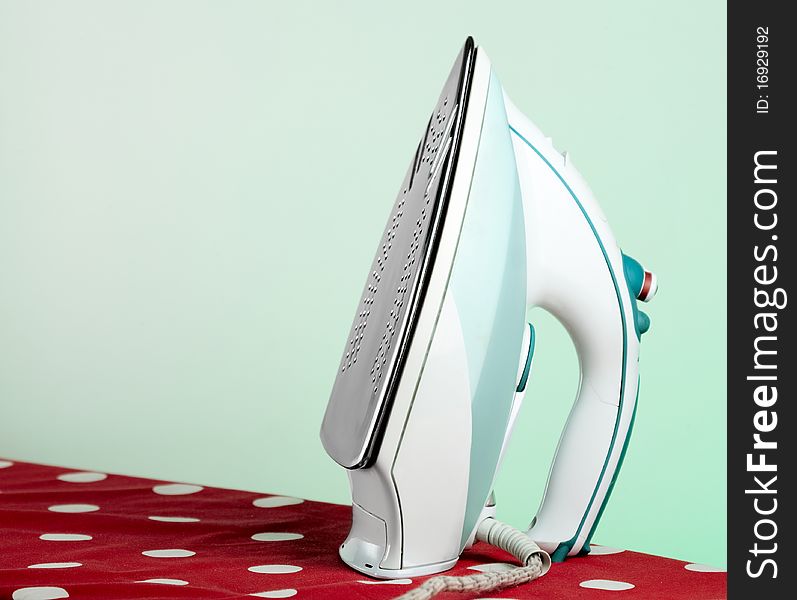 Modern electronic iron on an ironing board with green background